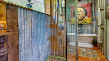 A rustic bathroom with a wooden shower enclosure, a vintage bathtub, and a colorful tiled floor.