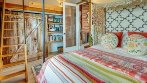 A bedroom with a wooden ladder, a bookshelf, a patterned bedspread, and a decorative headboard.