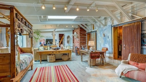 A spacious room with a large bed, a wooden desk, a dining table, and a sofa.