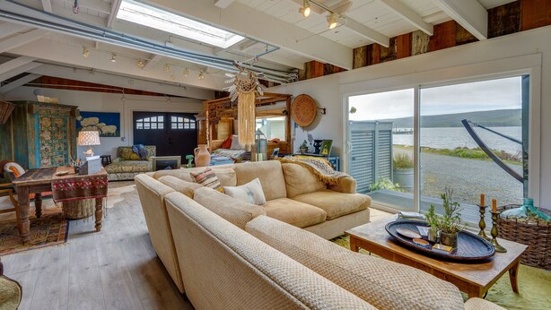 A spacious living room with a large beige sectional sofa, a wooden coffee table, and a view of a body of water through large windows.
