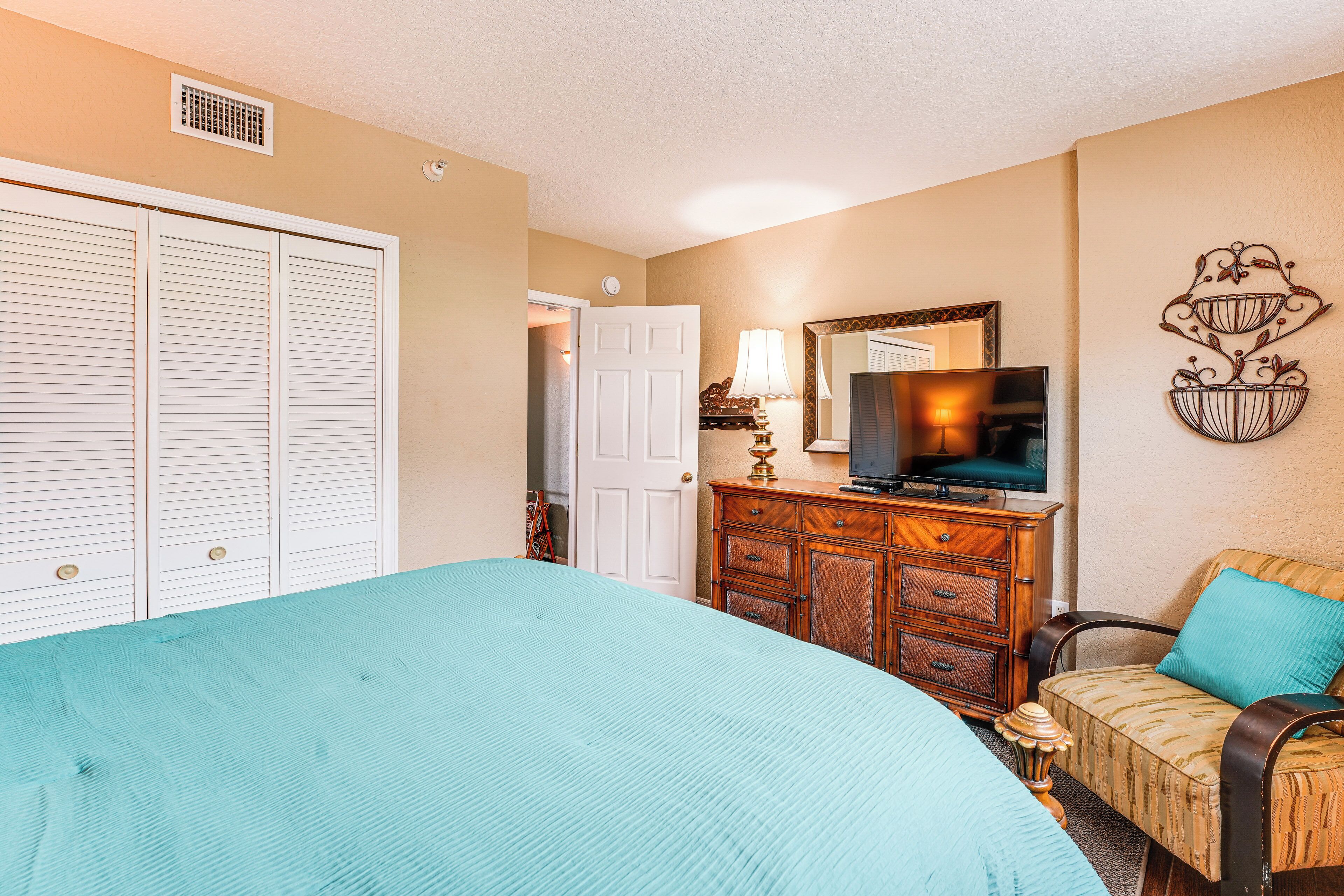 A bedroom with a large bed, a dresser, a television, and a chair.