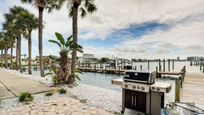 Een terras aan het water met een barbecue, gasflessen en palmbomen.