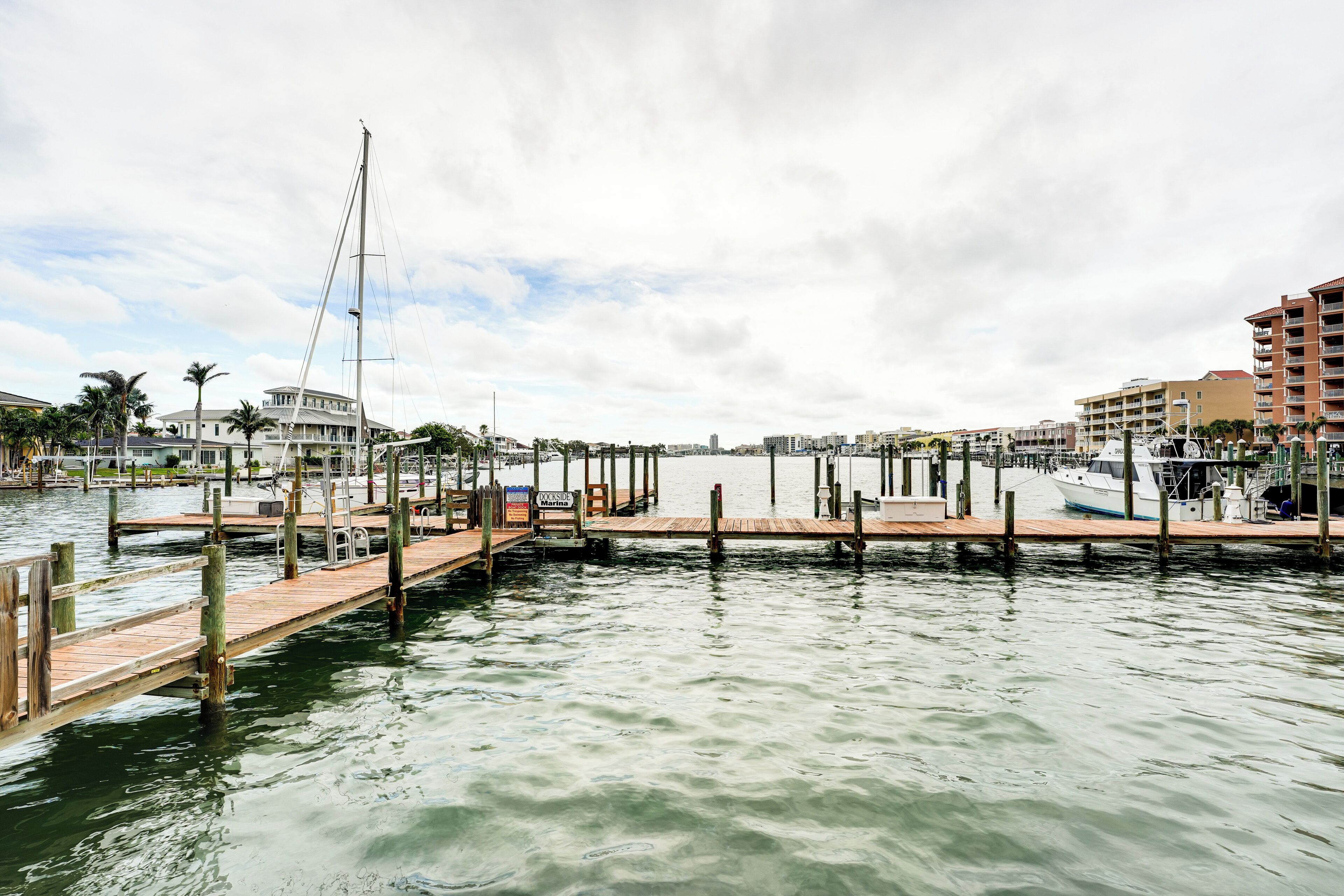 A marina with wooden docks, a sailboat, and buildings in the background.