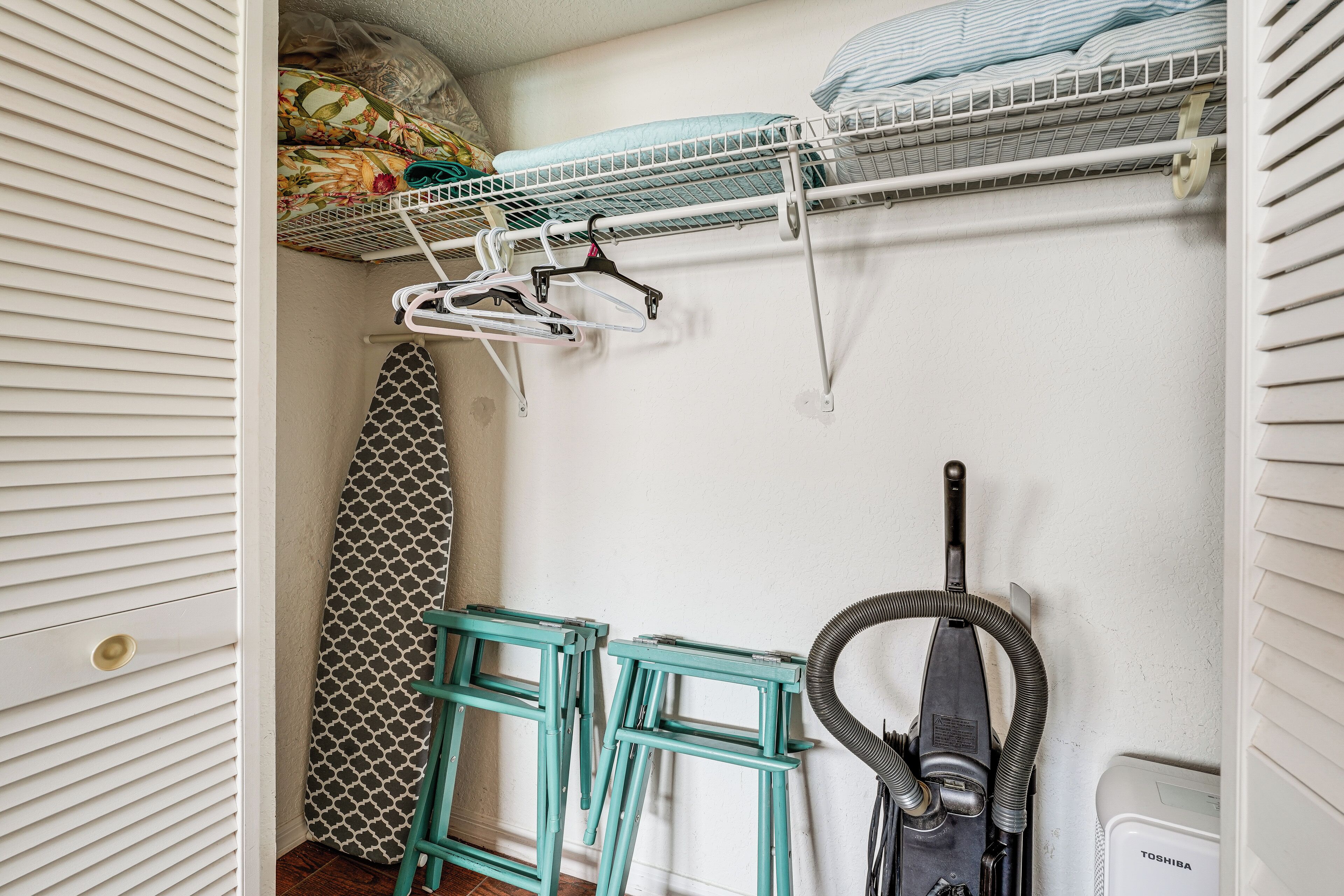 Habitación pequeña con una cama litera, un tendedero, un aspirador y una tabla de planchar estampada.