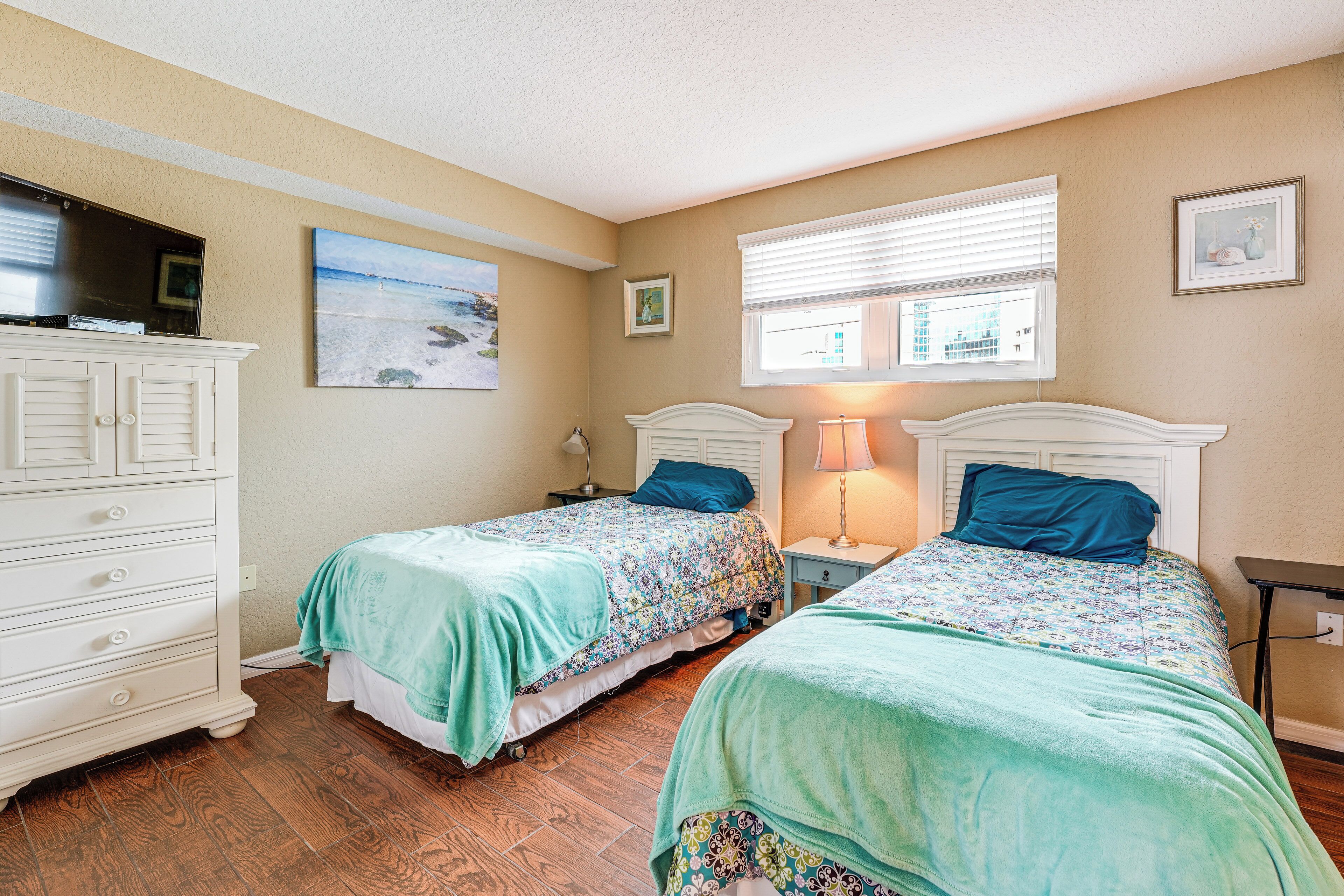 Une chambre avec deux lits, une commode et un téléviseur posé sur un meuble.