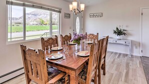 A dining room with a wooden table set for six, a chandelier, and a view of mountains through large windows. - Picturesque Palisade Home: Mt Garfield Views! (Palisade)