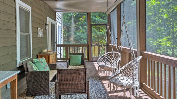 A covered porch with wicker furniture, a hanging chair, and a view of a forest. - Massanutten Family Retreat: Ski, Golf, & Hike! (McGaheysville)