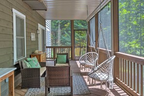 A covered porch with wicker furniture, a hanging chair, and a view of a forest. - Massanutten Family Retreat: Ski, Golf, & Hike! (McGaheysville)