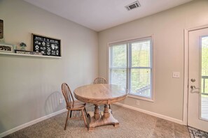 A dining area with a round wooden table and chairs, a window with blinds, and a wall-mounted shelf with framed pictures. - Massanutten Family Retreat: Ski, Golf, & Hike! (McGaheysville)