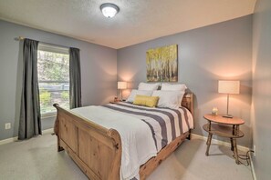 A bedroom with a wooden bed, two bedside lamps, a small round table, and a window with curtains. - Massanutten Family Retreat: Ski, Golf, & Hike! (McGaheysville)