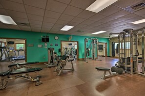 Une salle de sport équipée de divers appareils d’exercice, avec une horloge au mur et un mur vert.