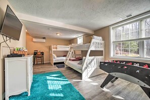 Une chambre avec des lits superposés, un baby-foot, un bureau avec un ordinateur et une fenêtre avec des stores.