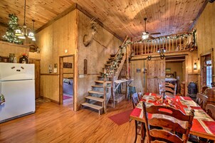 Un interior rústico de madera con comedor, escalera y cocina, que incluye un refrigerador.