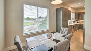 A modern dining area with a table set for four, a large window with blinds, and a kitchen in the background. - Bright & Spacious Houston Townhome: Near Dtwn (Houston)