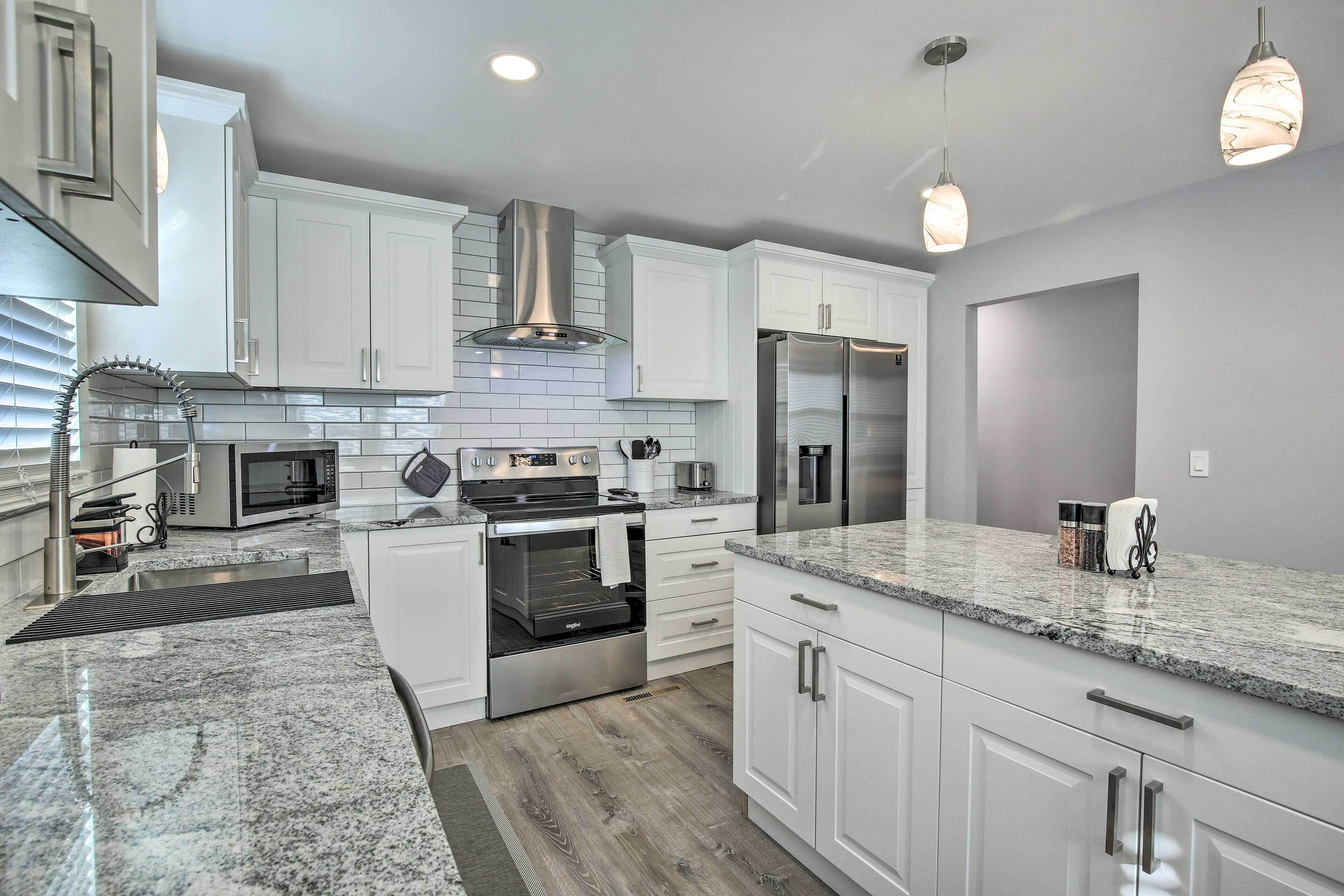 A modern kitchen with white cabinetry, stainless steel appliances, granite countertops, and pendant lighting.