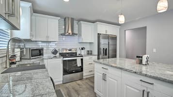 A modern kitchen with white cabinetry, stainless steel appliances, granite countertops, and pendant lighting.