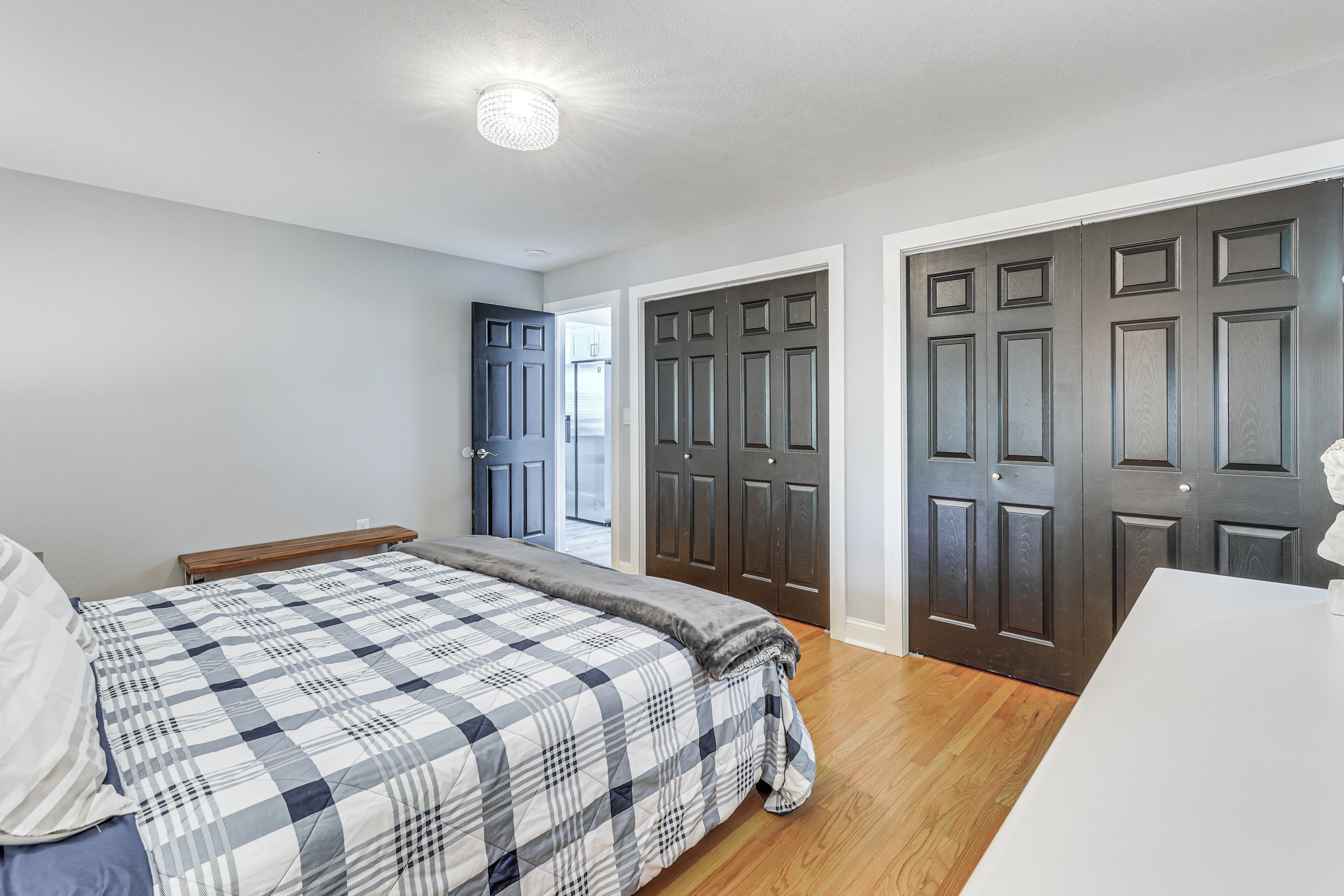 Un dormitorio con cama, mesita de noche, cómoda y una puerta que da a otra habitación.