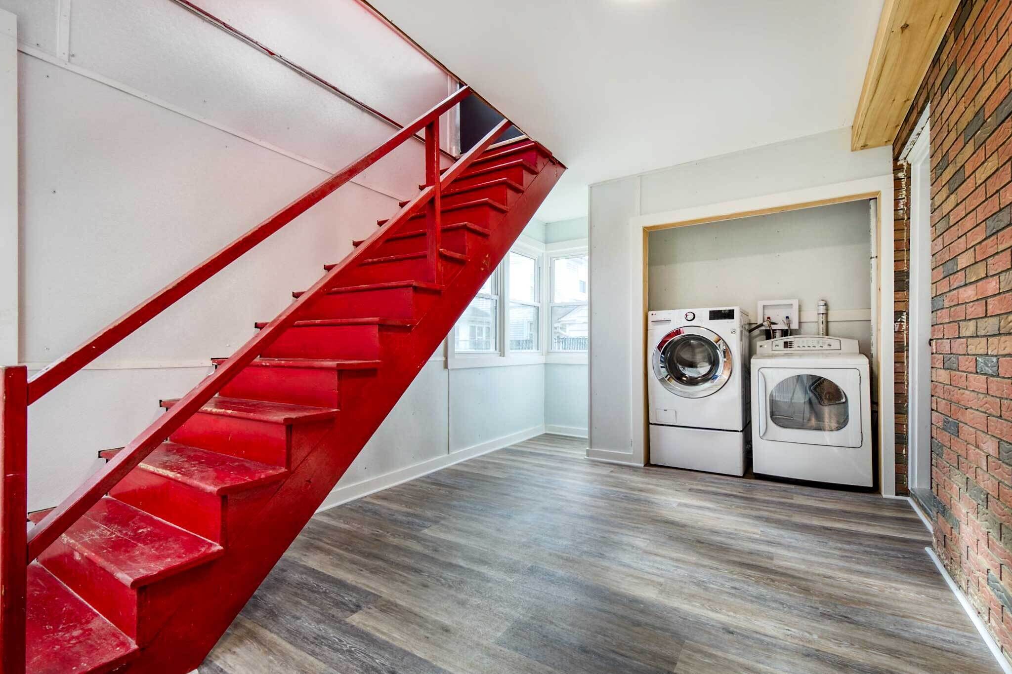 A modern apartment with a red spiral staircase, a laundry area with two washing machines, and a view of the outside through large windows.