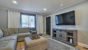 Een moderne woonkamer met een modulaire bank, een voetenbankje en een flatscreen televisie op een houten kast.