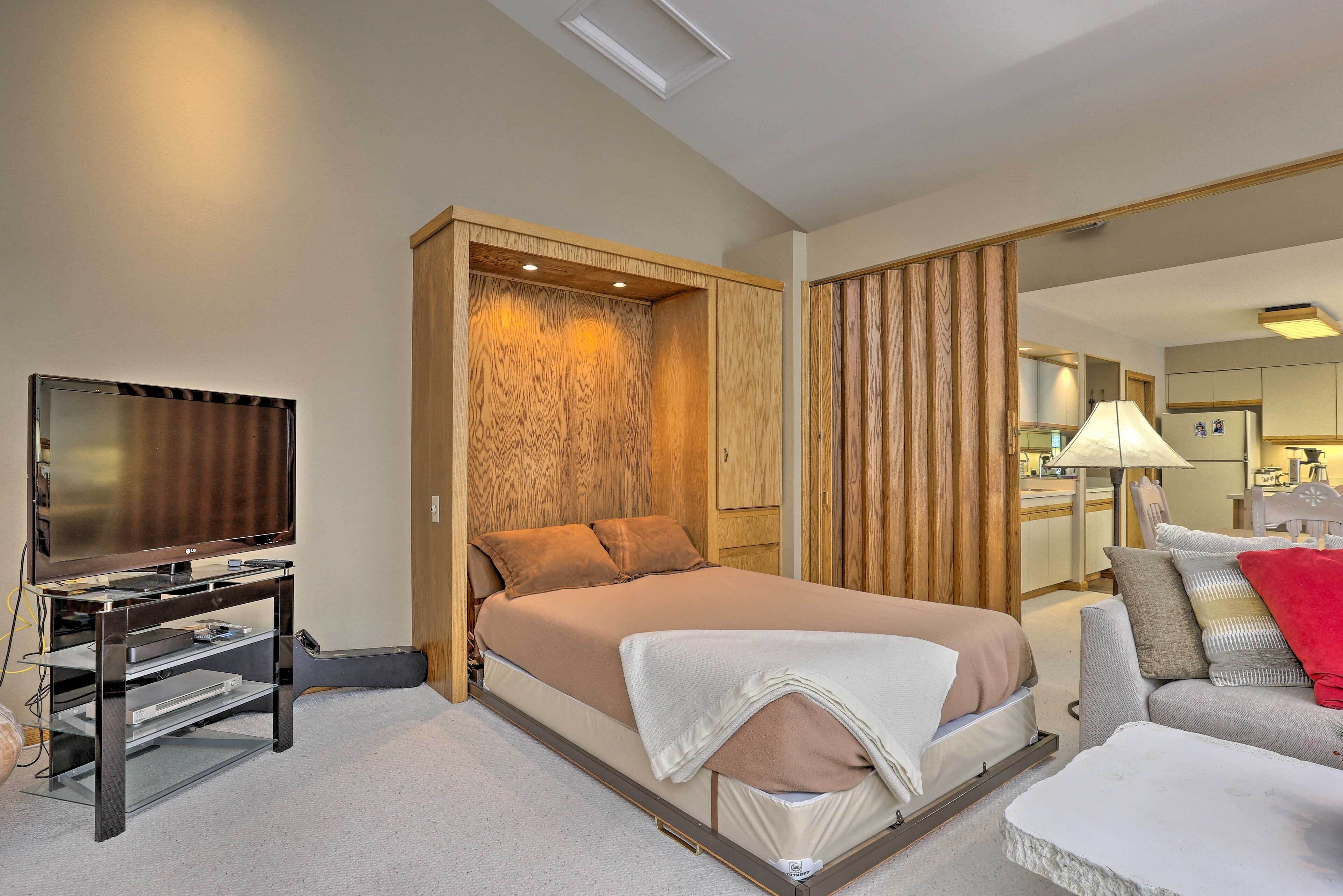 A hotel room with a bed, a television, a guitar, and a sofa.