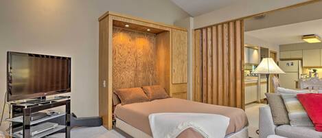 A hotel room with a bed, a television, a guitar, and a sofa.