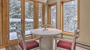 Ein Zimmer mit einem runden Tisch und vier Stühlen, großen Fenstern mit Holzrahmen und Blick auf eine verschneite Landschaft.