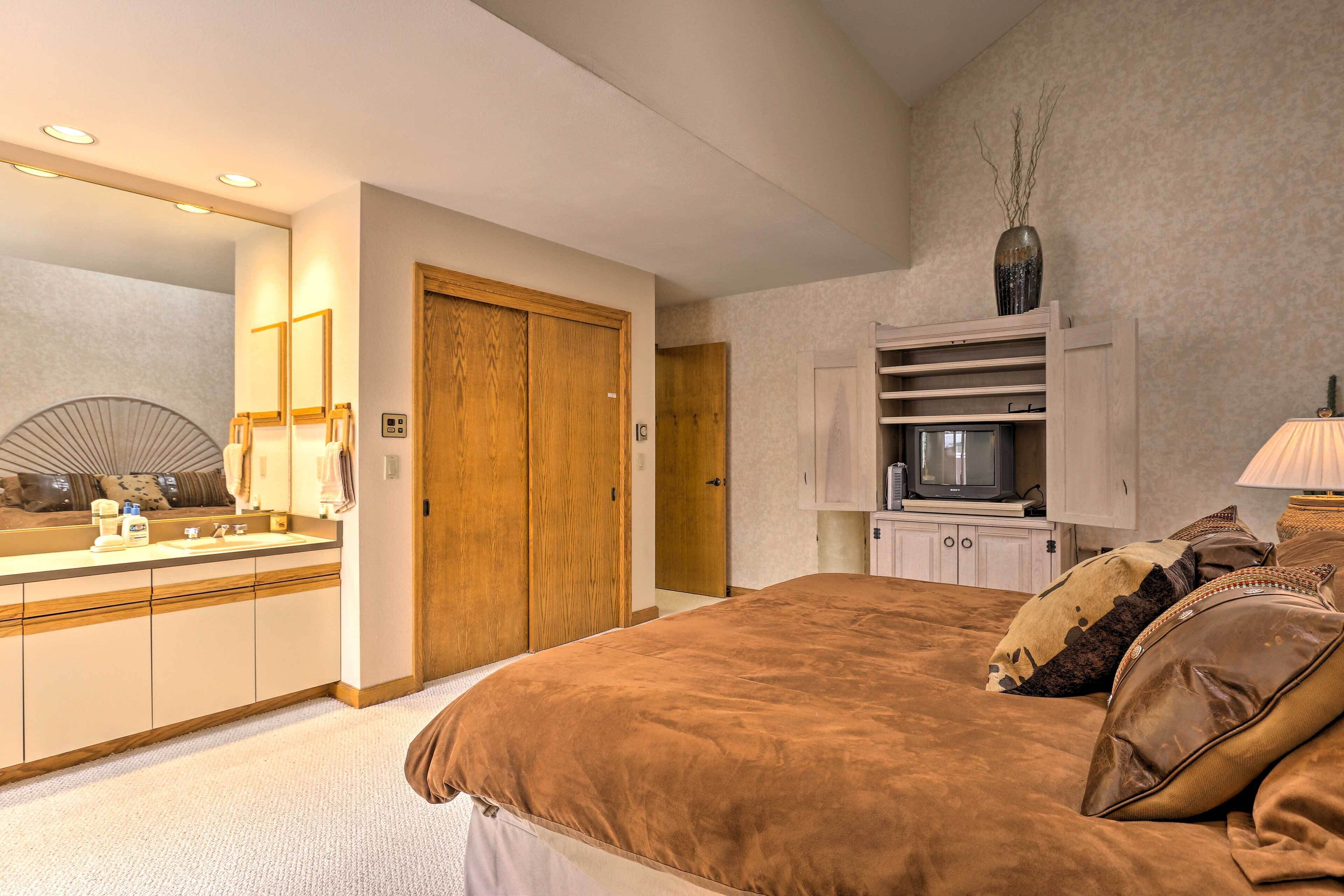 A bedroom with a large bed, a wooden wardrobe, a television, and a mirror.