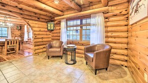 Interior de una cabaña de troncos con paredes de madera, un comedor con mesa y sillas, y dos sillones de cuero.