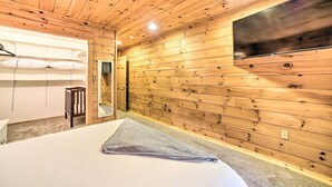 Una habitación con paneles de madera, una cama, una cuna, un espejo y un televisor montado.