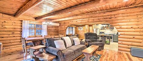 A log cabin interior with a sofa, coffee table, and dining area.