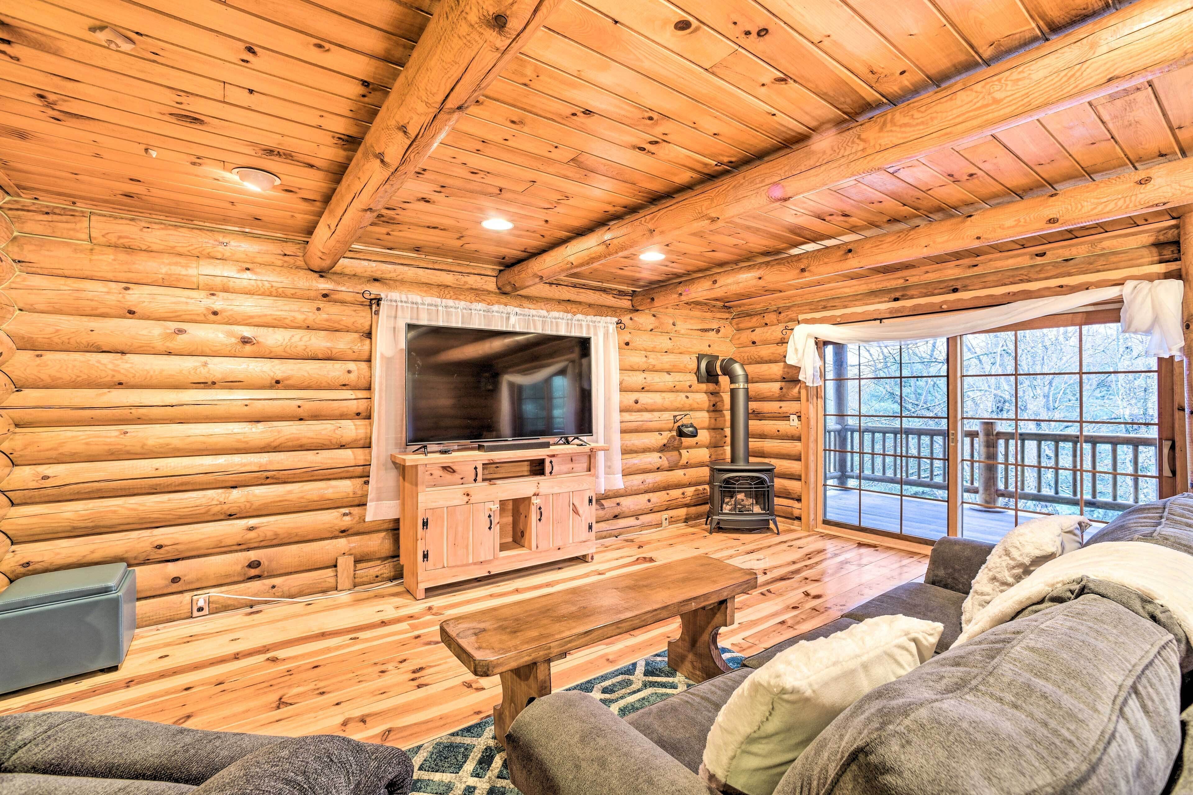 A log cabin interior with a wooden floor, a sofa, a television, a fireplace, and a large window.