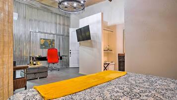 Une chambre avec une couvre-lit à motifs, un plaid jaune, un bureau avec une chaise, une carte accrochée au mur et un téléviseur fixé au mur.