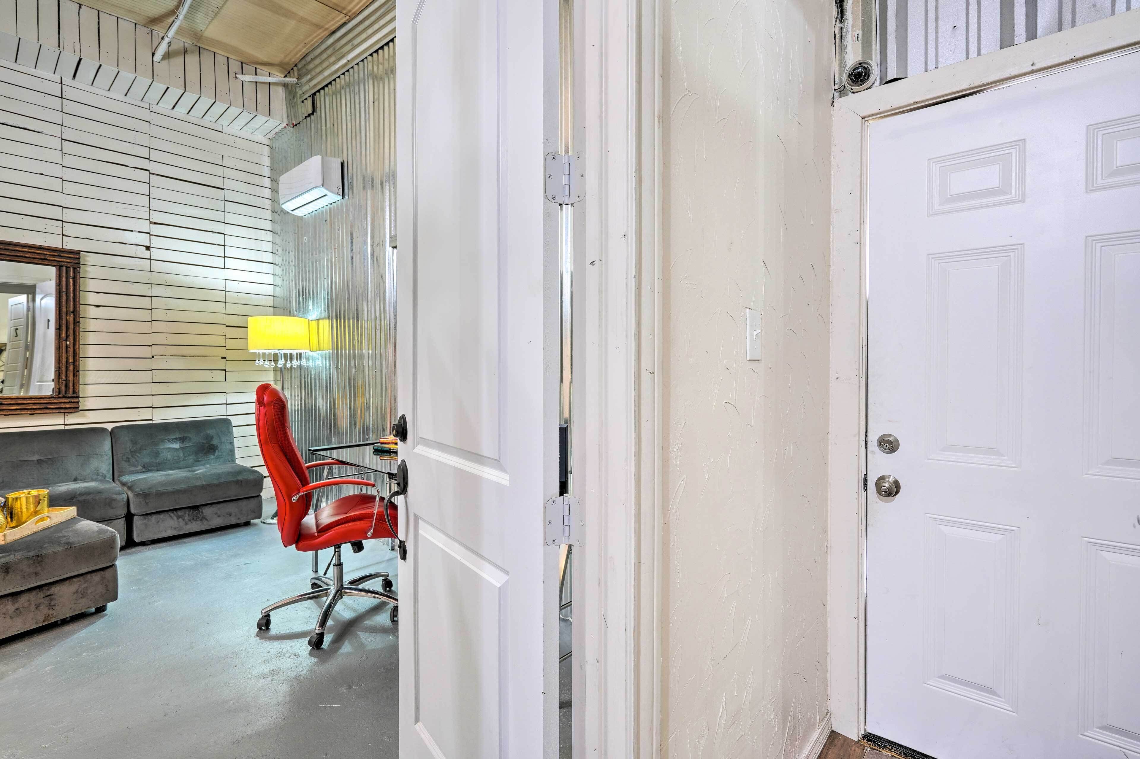 Una stanza con una porta bianca, una sedia da ufficio rossa, un divano e una lampada.