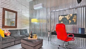 A modern office space with a grey sofa, a red office chair, a small table with decorative items, a world map on the wall, and a metal-framed window. - Ideally Located Vacation Rental Studio in Laredo! (Laredo)