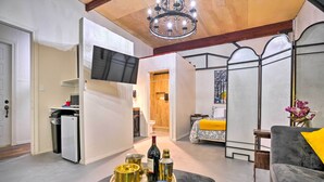 A modern living room with a grey sofa, a wooden coffee table with drinks, a TV mounted on the wall, and a chandelier. - Ideally Located Vacation Rental Studio in Laredo! (Laredo)
