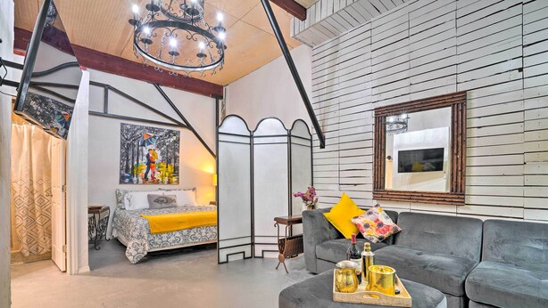A modern living room with a grey sofa, a small coffee table with decorative items, a bed with patterned bedding, and a large painting on the wall. - Ideally Located Vacation Rental Studio in Laredo! (Laredo)