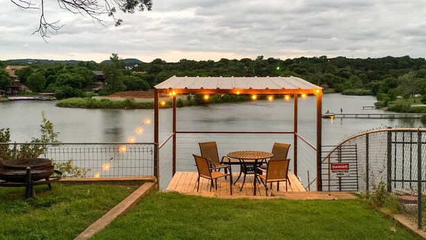 Een prieeltje met lichtslingers, een tafel en stoelen met uitzicht op een meer.