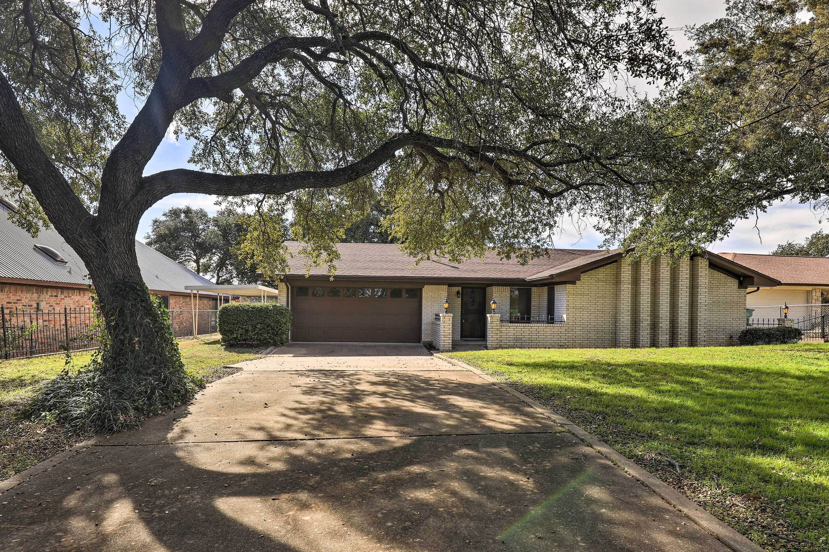 A residential house with a front yard, a driveway, and a large tree providing shade.