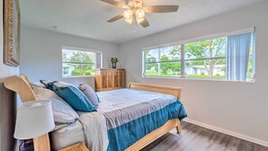 Ein Schlafzimmer mit Bett, Deckenventilator, Nachttisch, Fenster und Blick ins Freie.