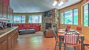 A spacious living area with a stone fireplace, a dining table with chairs, and a red couch. - Unique Gatlinburg Cabin: Decks, Hot Tub, Fire Pit (Gatlinburg)