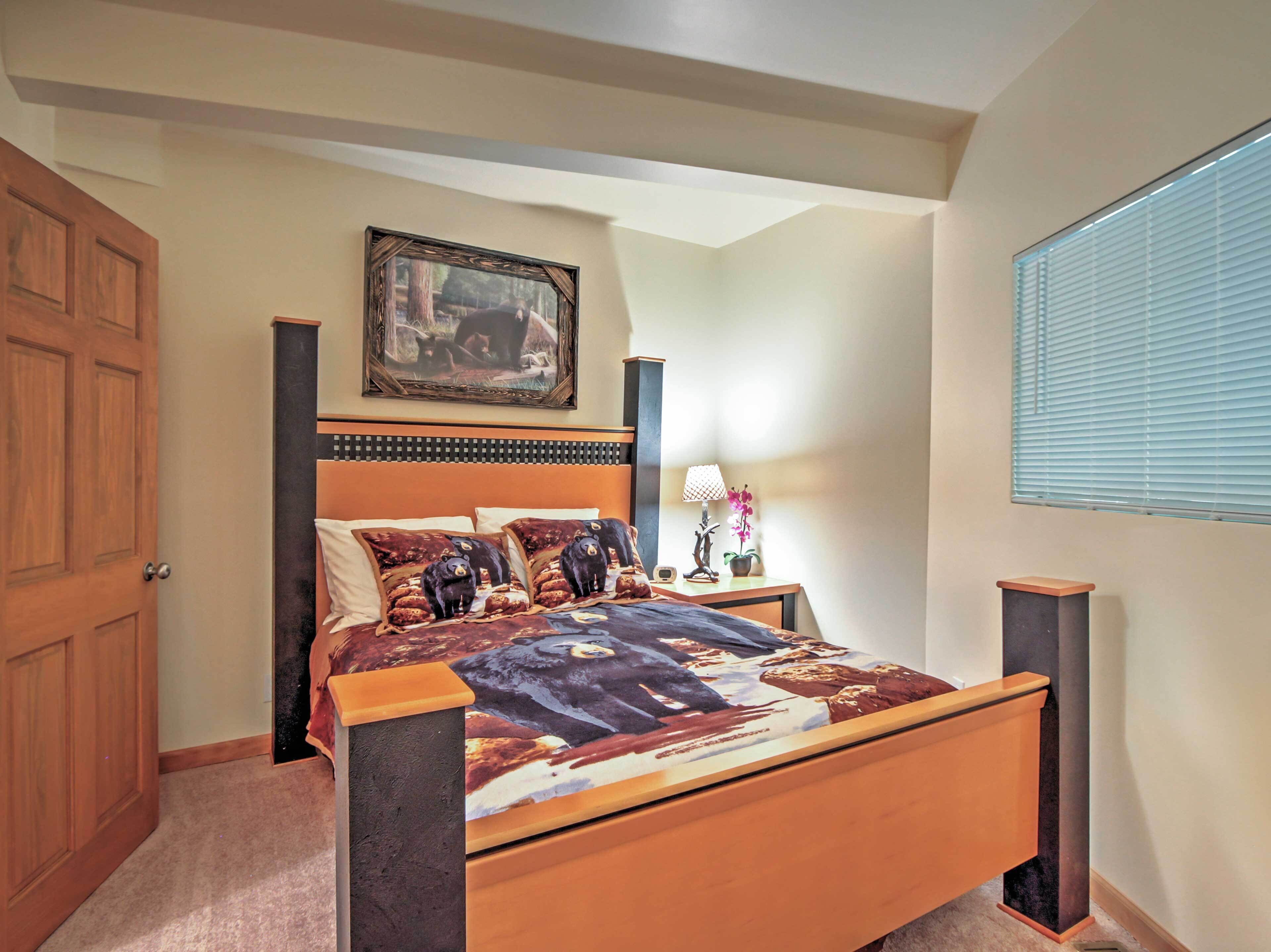 A bedroom with a wooden bed, a painting above the bed, a nightstand with a lamp, and a window with blinds.