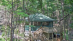 A wooden cabin with a green roof, surrounded by trees. It features a wooden deck and a hot tub. - Unique Gatlinburg Cabin: Decks, Hot Tub, Fire Pit (Gatlinburg)