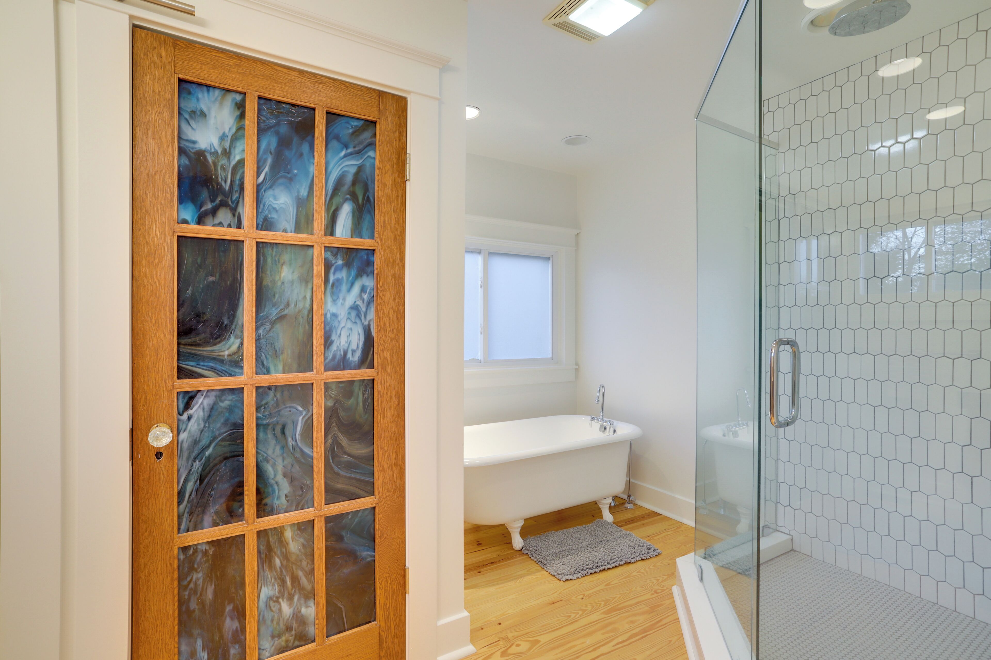 Un baño con cabina de ducha de vidrio, una bañera blanca y una puerta de madera con paneles de cristal.
