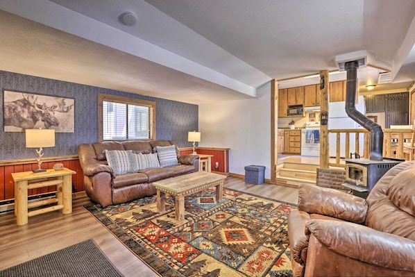 A cozy living room with a brown leather sofa, a wooden coffee table, and a patterned rug. A fireplace is visible in the background, and wooden cabinets line the walls.