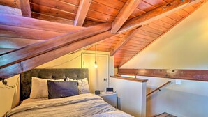 A bedroom with a sloped ceiling, a bed with multiple pillows, a bedside table, and a nightstand. - Waterfront Clearlake Retreat w/ Dock & Kayaks (Clearlake)