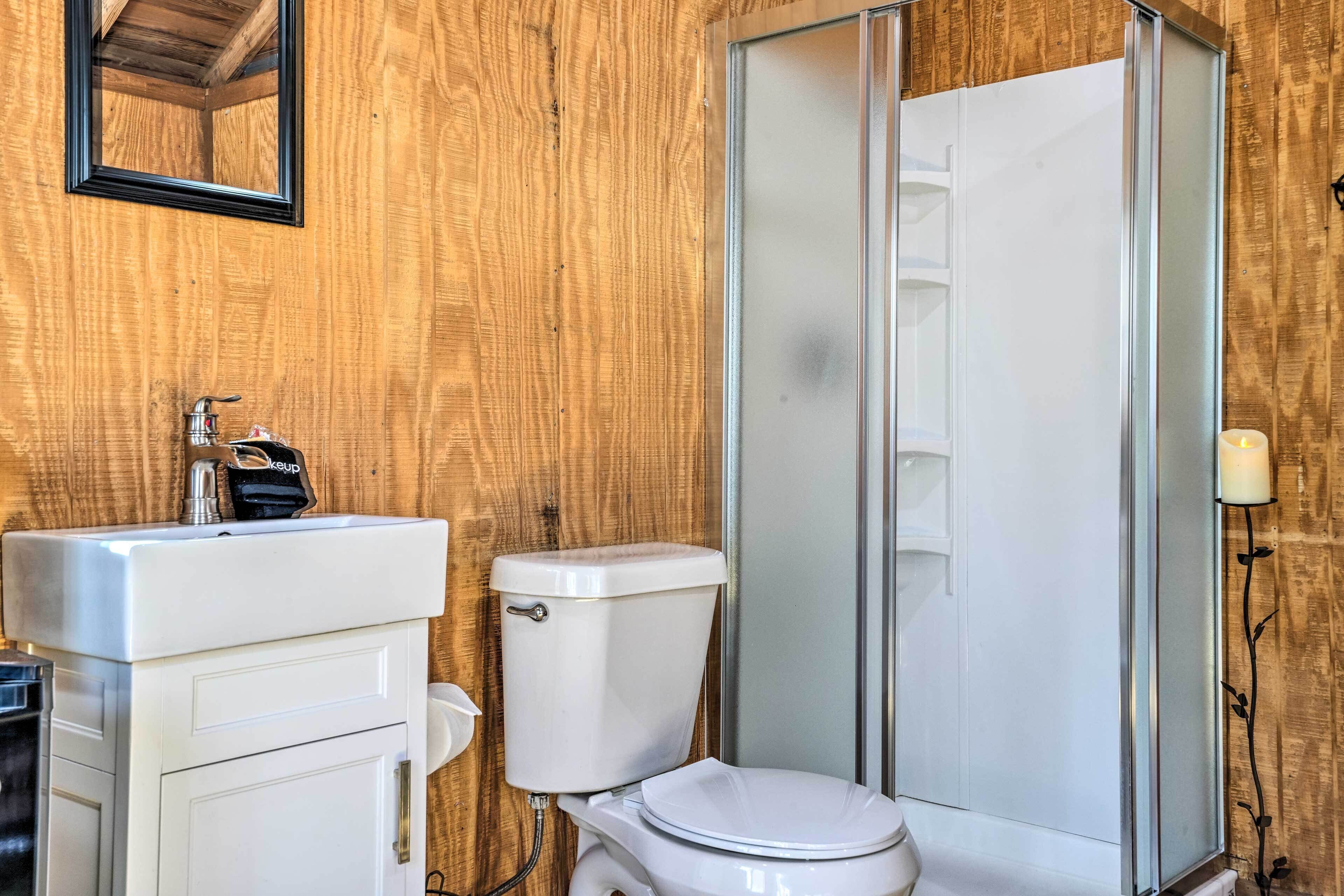 Un baño con pared de madera, un lavamanos blanco, un inodoro y una mampara de cristal para la ducha.