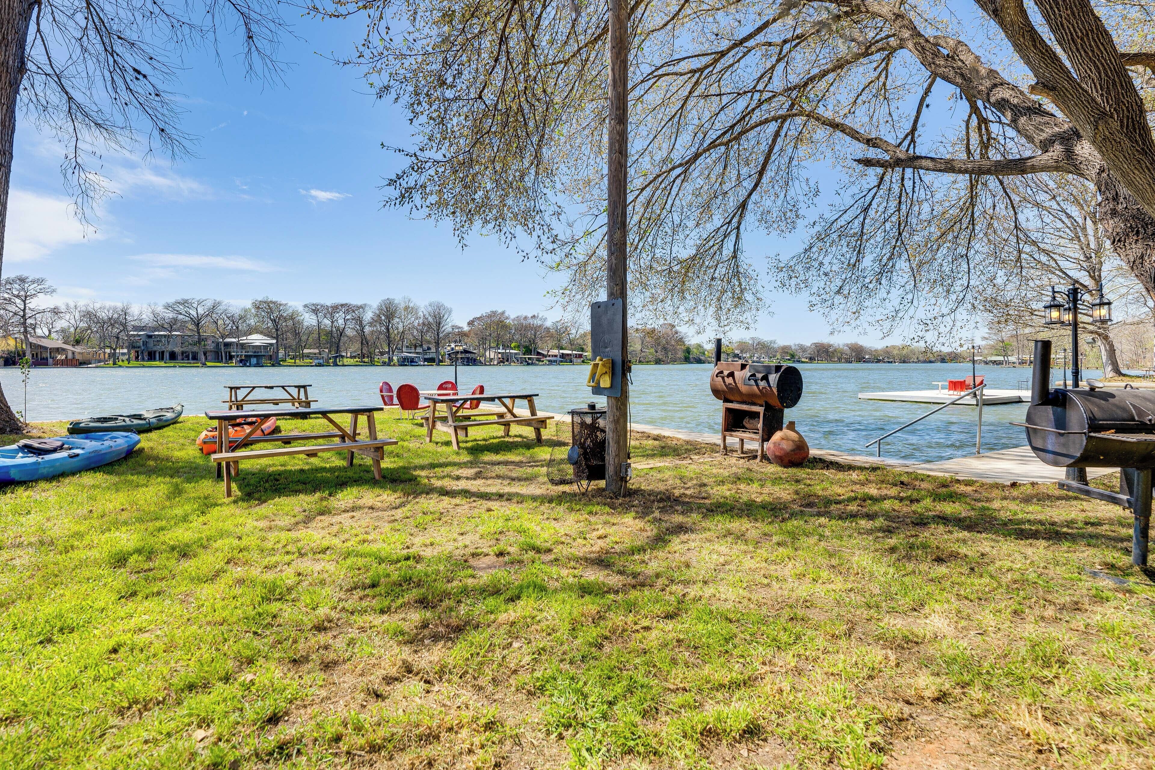 Zona de pícnic a la vora del llac amb taules de pícnic, una barbacoa, kayaks i vista a l'aigua.