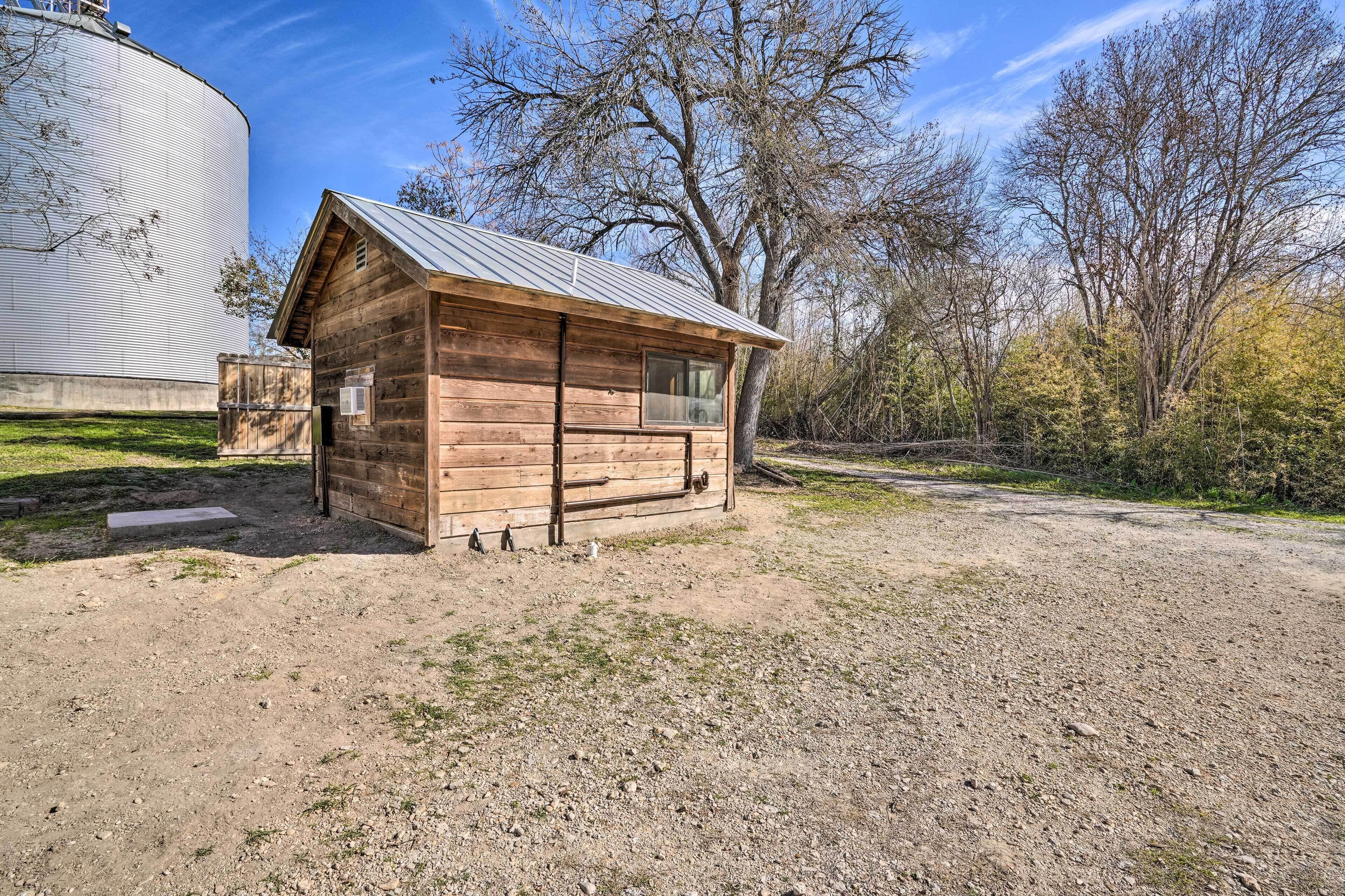 A rustic wooden cabin with a metal roof, situated on a gravel path with trees in the background.