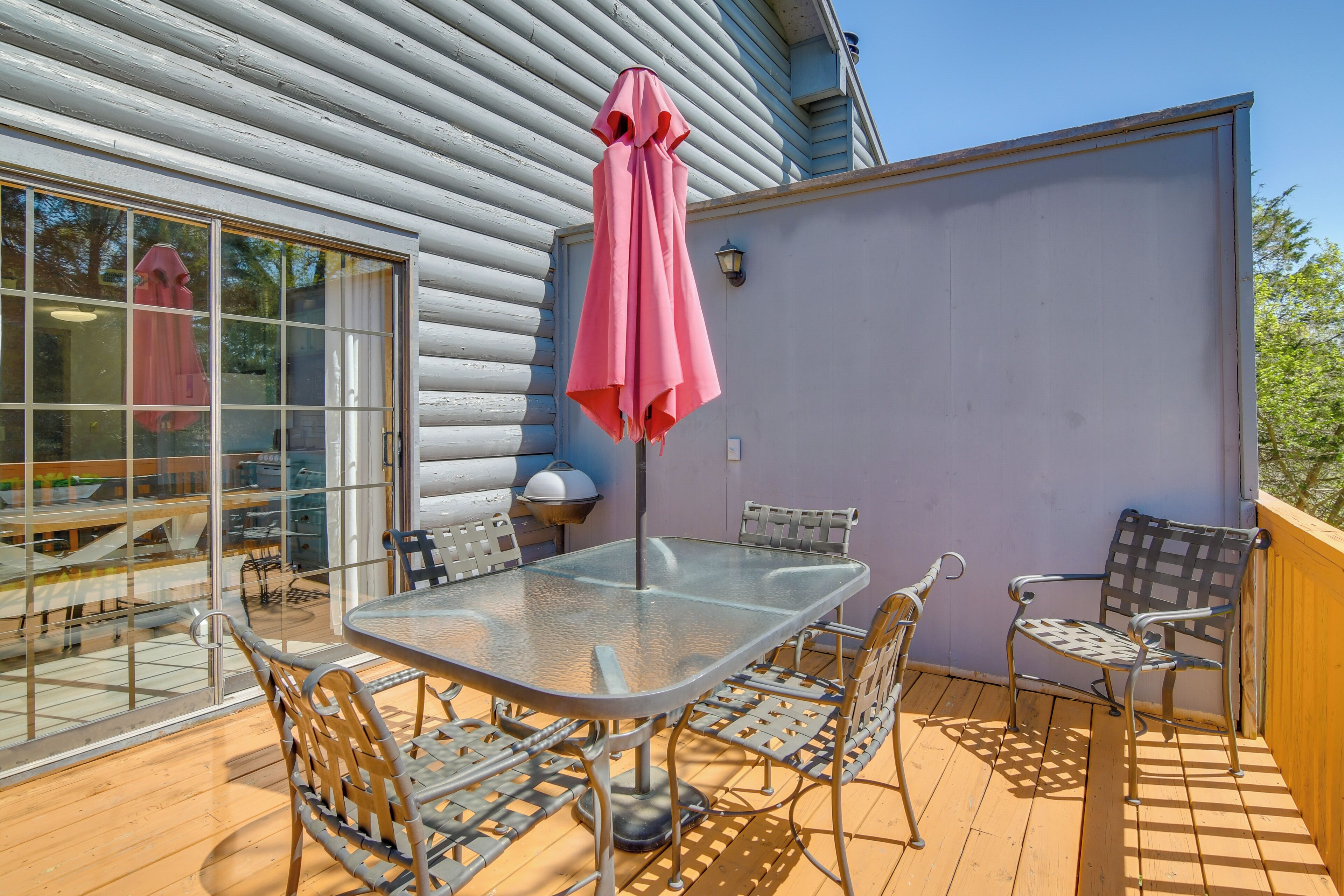 Eine überdachte Terrasse im Freien mit einem Glastisch, Metallstühlen und einem pinkfarbenen Sonnenschirm.