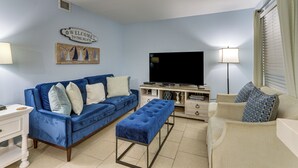 A living room with a blue sofa, a beige sofa, a blue bench, a flat-screen TV, and a 'Welcome to the Beach' sign. - Beach & Pool Access: Hilton Head Resort Condo (Hilton Head Island)
